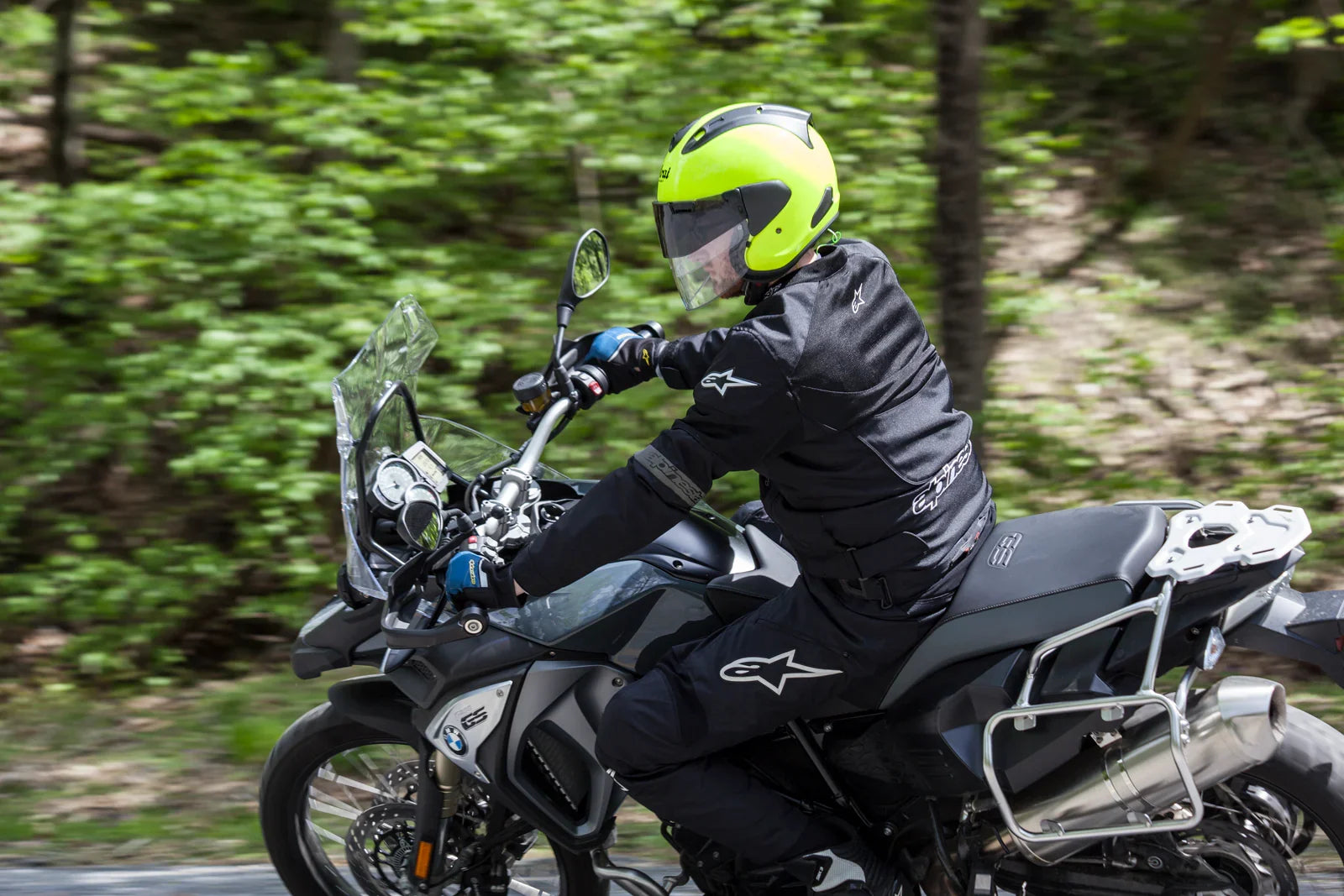 Rider in neon yellow helmet and black gear on adventure motorcycle through forest